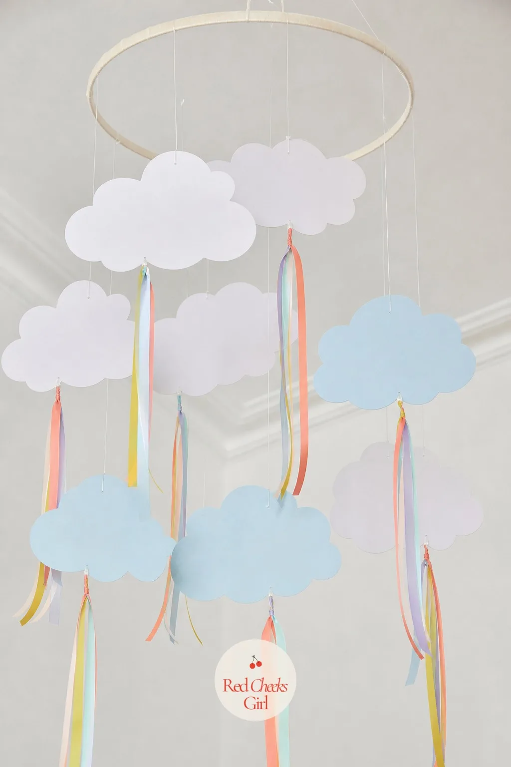 A Paper Cloud Mobile Overhead — Felt or card stock clouds in white and pale blue get cut, then threaded onto fishing line at different lengths so they hang at