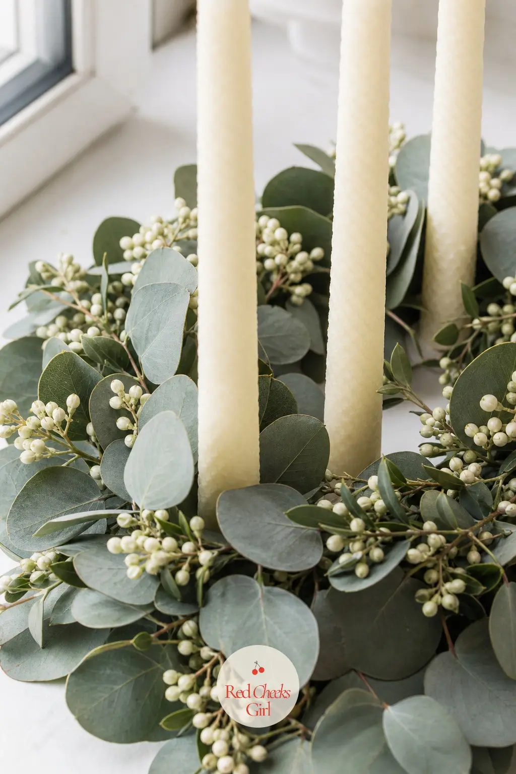 An All-White Beeswax Ring on Silver Dollar Eucalyptus and Privet Berry — Four plain white beeswax tapers sit in a low ring of silver dollar eucalyptus and