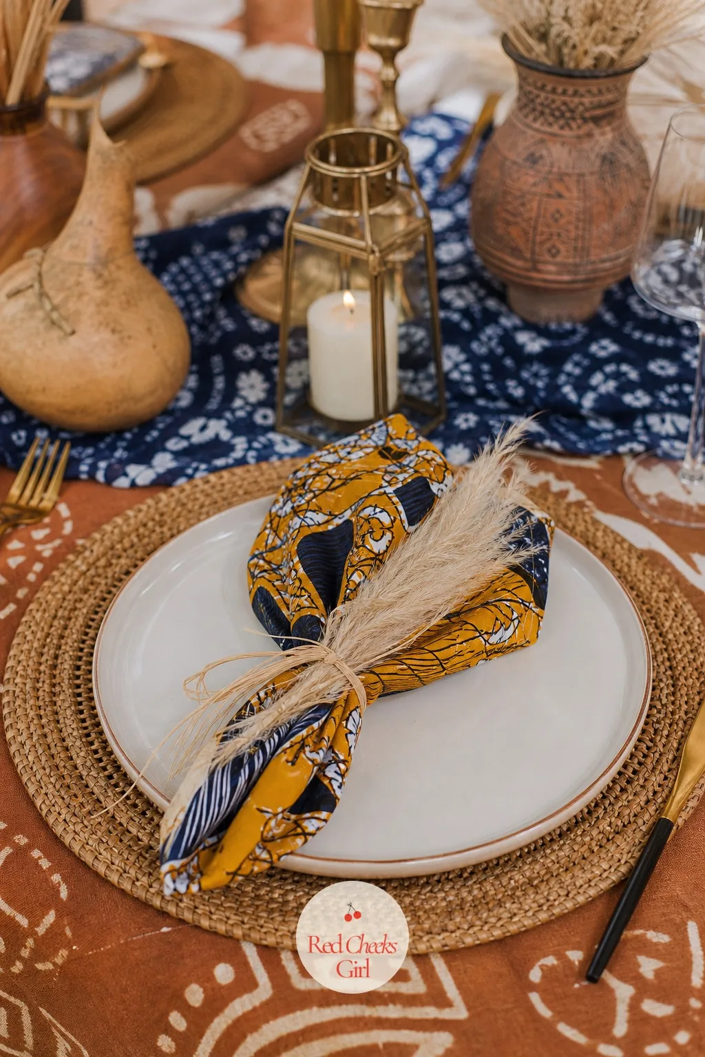 Rattan Chargers Under Wax-Print Napkins — Each place setting starts low and builds up: a round woven rattan charger on the table, a plain ivory dinner plate