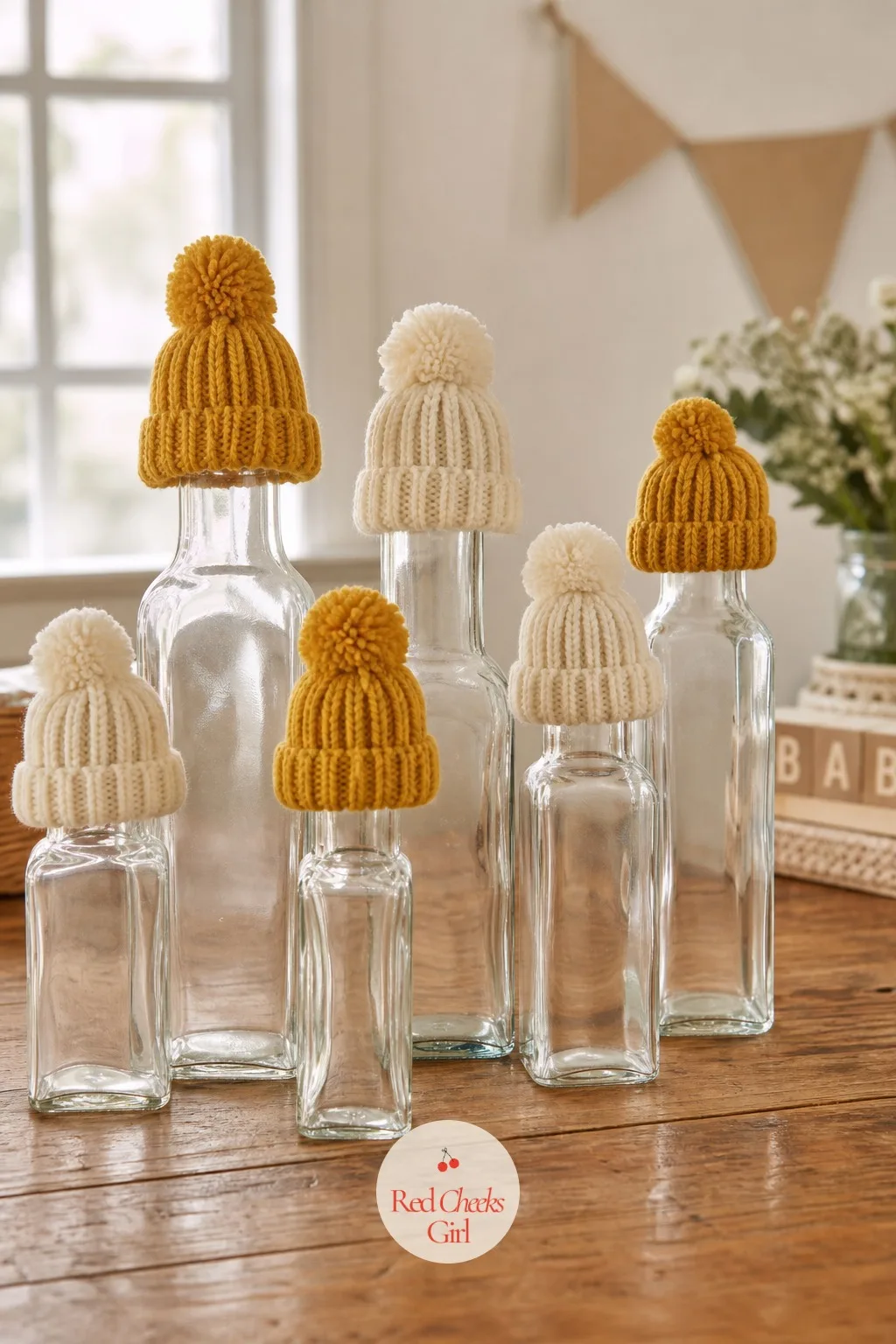 Baby Hats on Bottles — Knit baby hats, mustard and cream, sit perched on top of tall glass bottles the way a hat sits on a head, lined up in a short row that