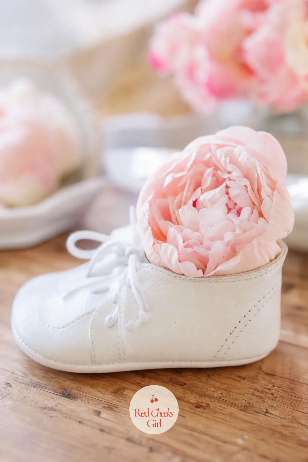 Baby Shoes Holding Flowers — A single white leather baby shoe, laid on its side, cradles one blush peony head in its open top as though it had been set down