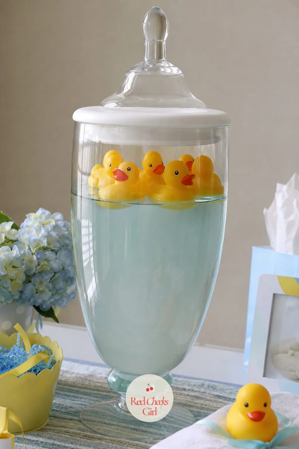 Bath Toys in an Apothecary Jar — A tall white apothecary jar filled with yellow rubber ducks, submerged in water tinted the softest blue, looks like something