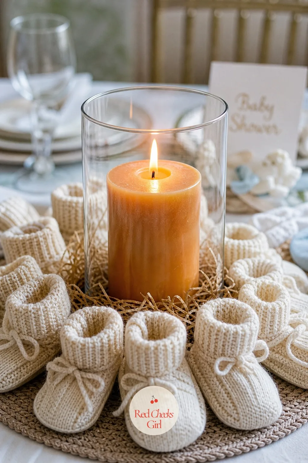 Knit Booties Around a Candle — A ring of cream knit booties circles a single amber pillar candle, toes pointed inward so the pair almost meets in the middle