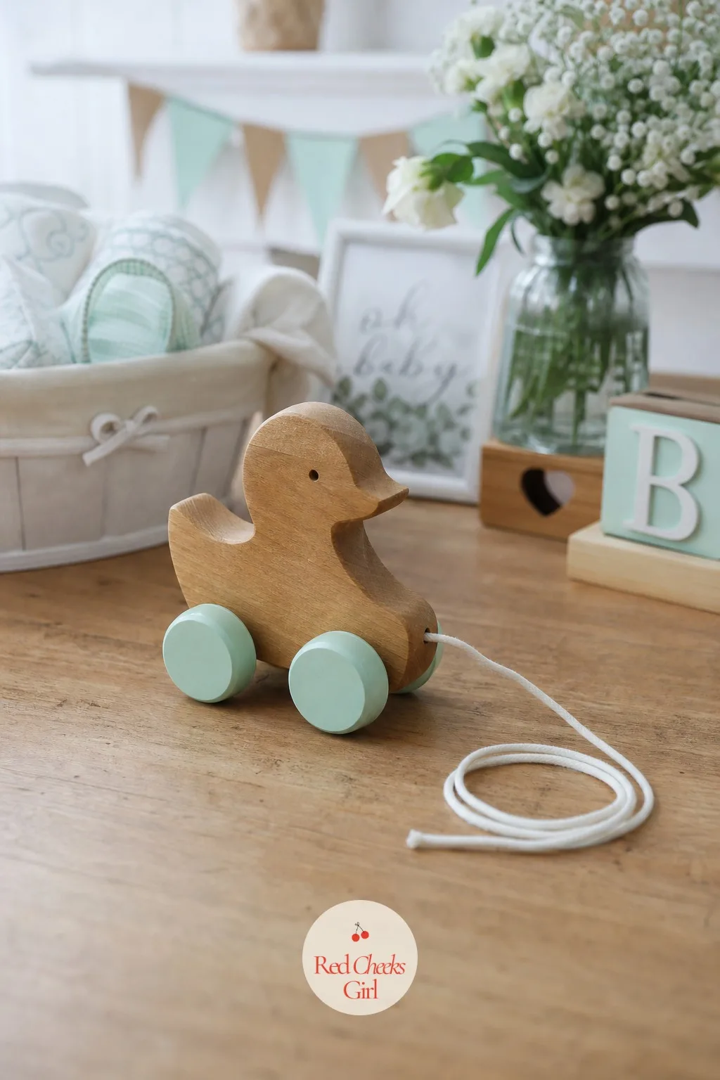 Wooden Pull Toy — A honey-wood duck pull toy, mint-painted wheels and a length of cord trailing behind it, sits on the table exactly as it would on a nursery
