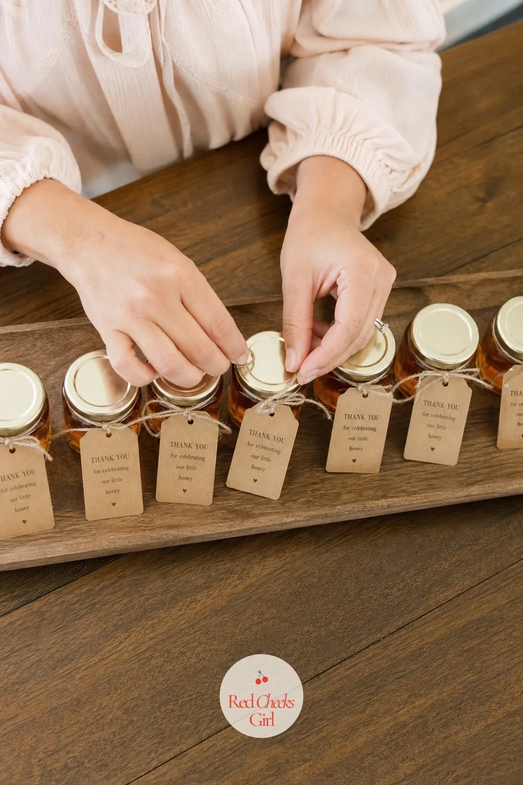 Prepare the Favors a Guest Will Actually Use — A row of small glass jars filled with honey sits lined up on a tray, each one tied with a plain tag and nothing