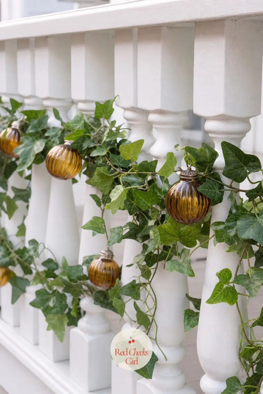 A Trailing Ivy and Amber Glass Bauble Garland Threaded Through the Balusters — Thread a faux ivy garland horizontally through the uprights rather than draping