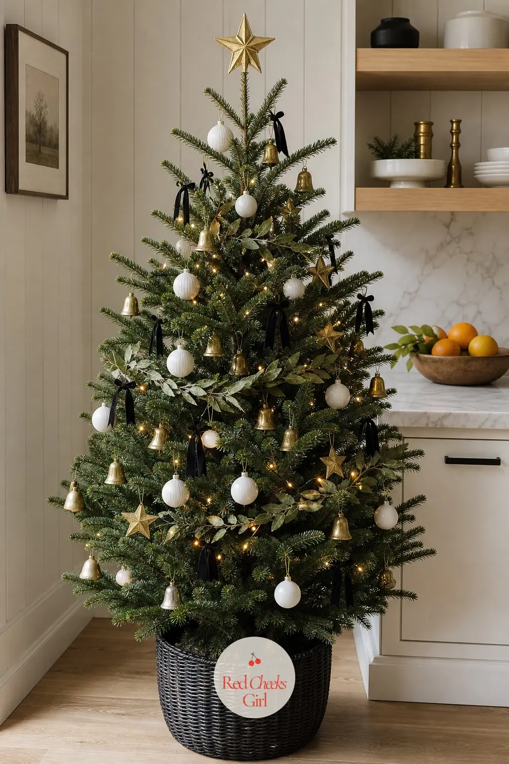 A Brass and Black Tree on the Marble Counter — On a marble counter in a white kitchen, beside open shelves and a bowl of citrus, this small real potted tree
