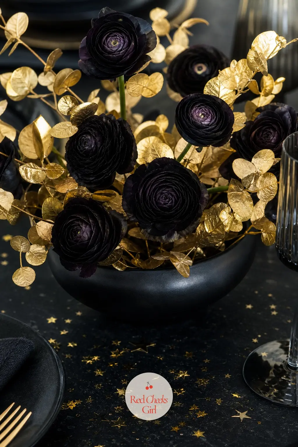 The Table Centerpiece, a Low Bowl of Black Ranunculus and Gold Leaf — A low black ceramic bowl holds near-black ranunculus and a few stems of gilded eucalyptus