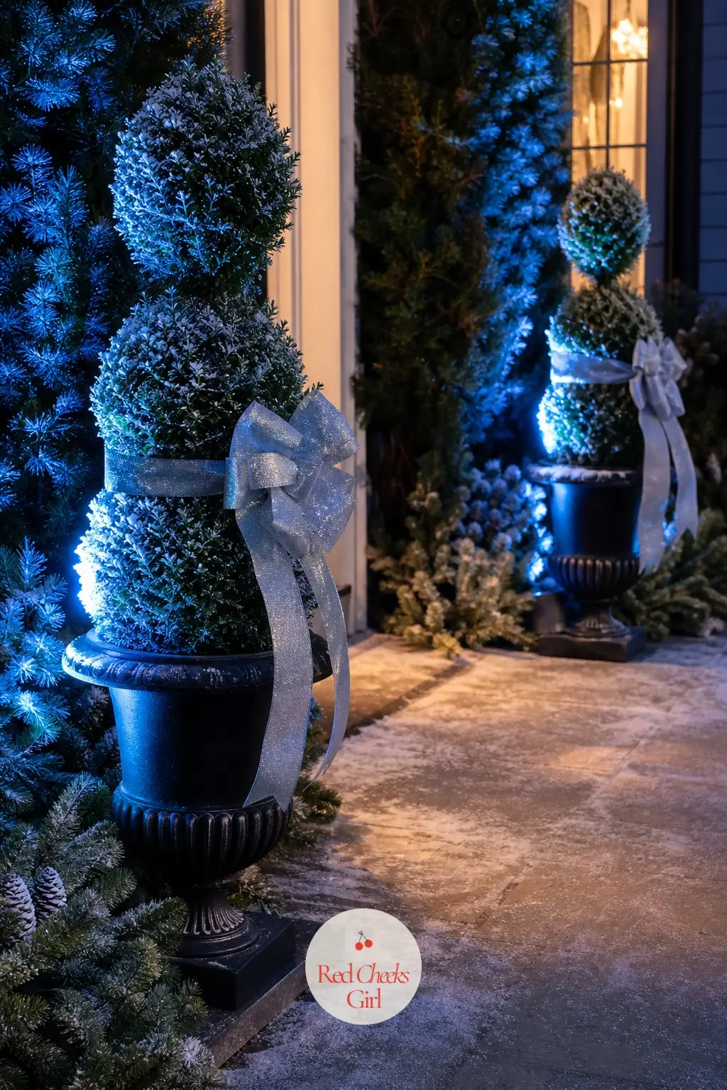 The Front Walkway, Lined With Frosted Topiaries — A pair of faux topiaries flanks the path in iron urns, dusted with a fine faux frost and tied at the trunk
