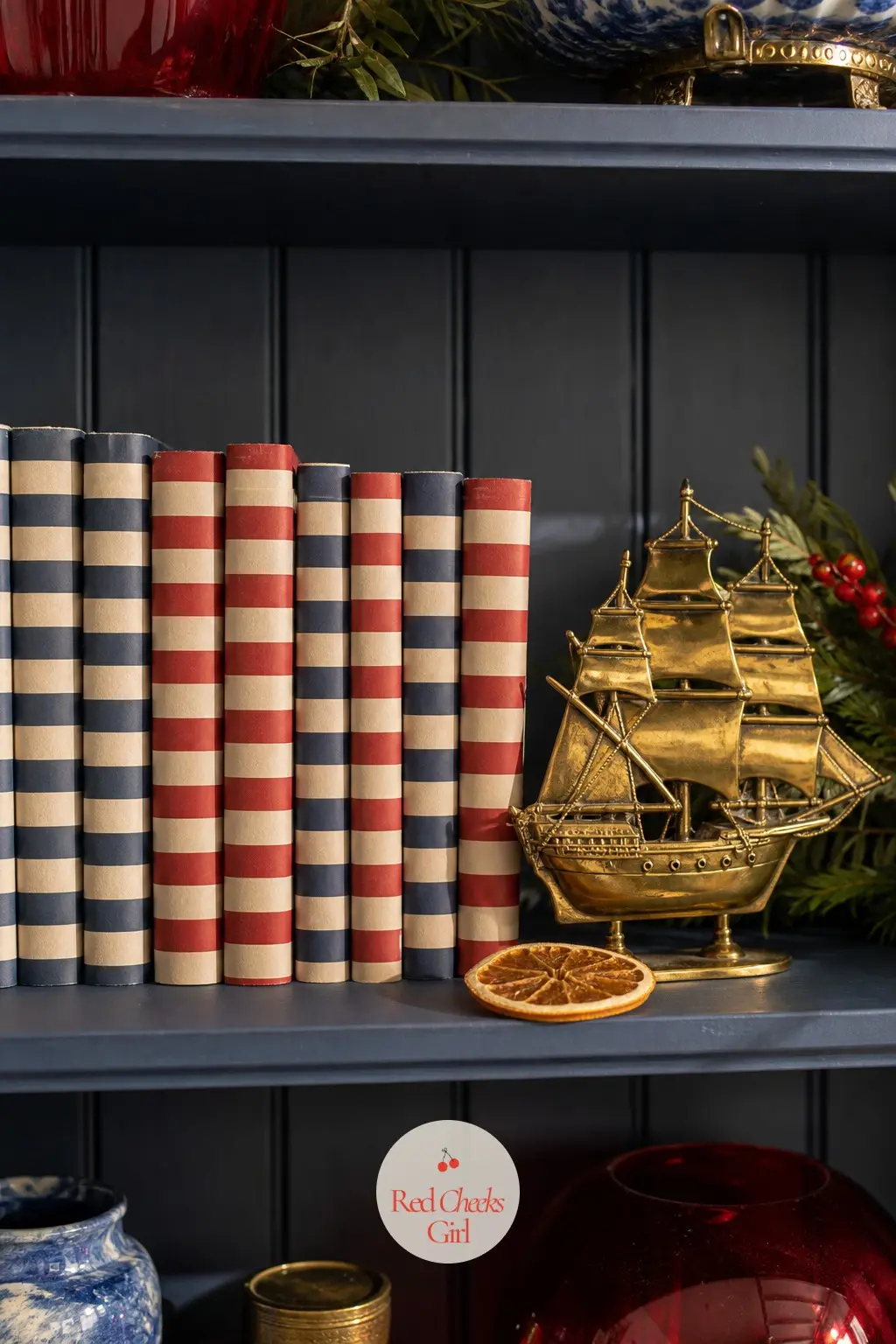 The Bookshelf, Styled With Striped Spines and a Brass Ship — A single open shelf gets a run of books rebound or simply sleeved in navy and cherry striped