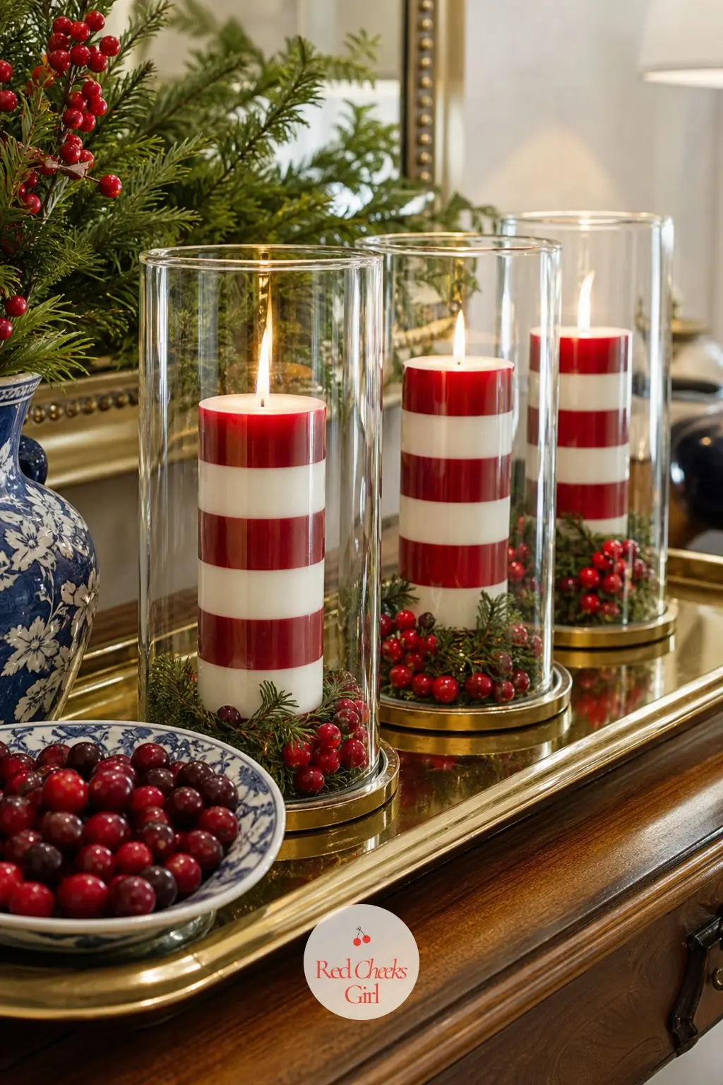 The Console Table, Set With a Row of 3 Striped Hurricane Lamps — Three glass hurricane lamps stand in a row on the entry console, each holding a thick striped