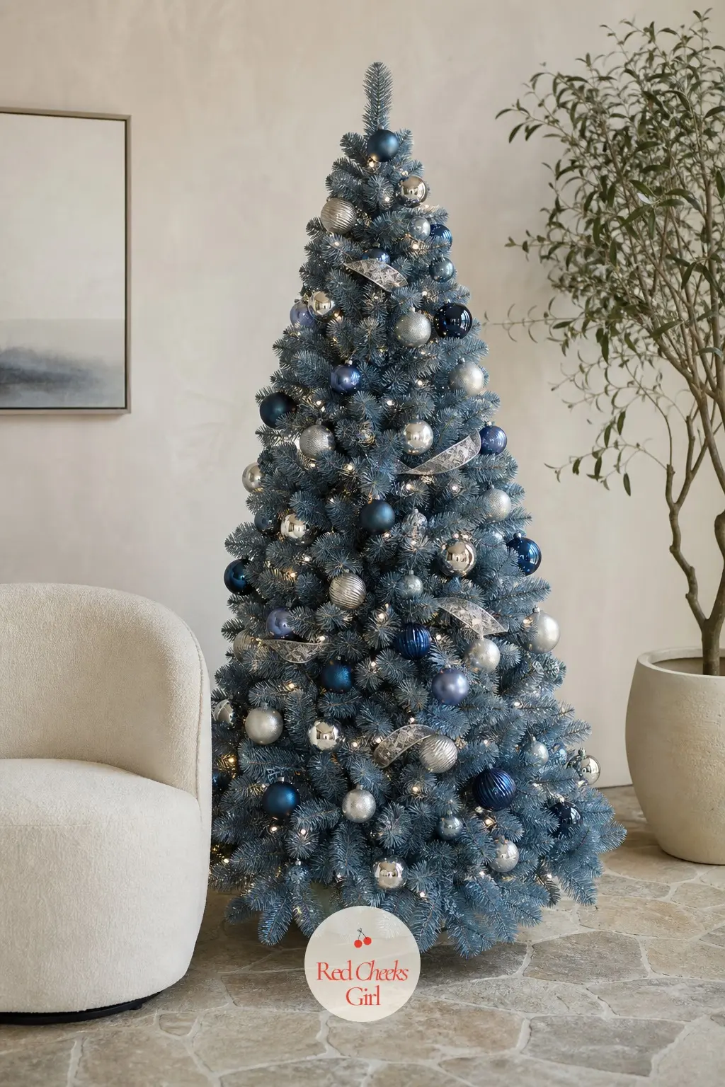 A Sculptural Steel Blue Tree by the Curved Chair — A full artificial tree standing beside a curved cream chair on a stone floor, steel blue baubles mixed