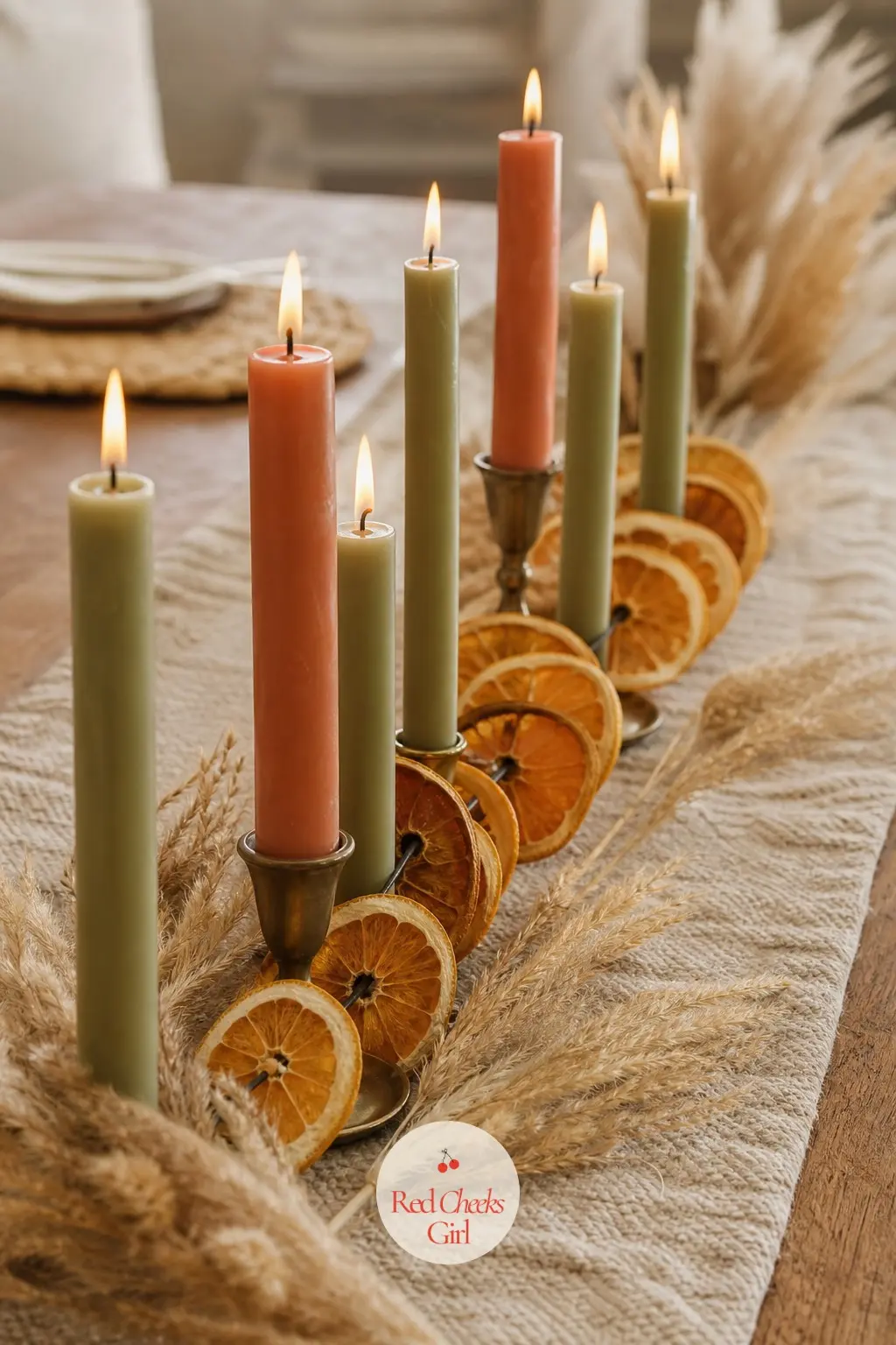 The Centerpiece of Candles and Dried Citrus — A low run of taper candles in terracotta and sage sits in brass holders down the table center, kept short enough