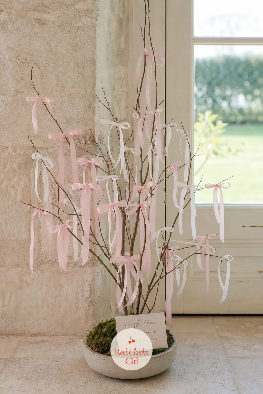 Ribbon Wish Tree — A few bare branches, weighted upright in a low vase of sand or stones, stand near the door with a small basket of thin pastel ribbon strips