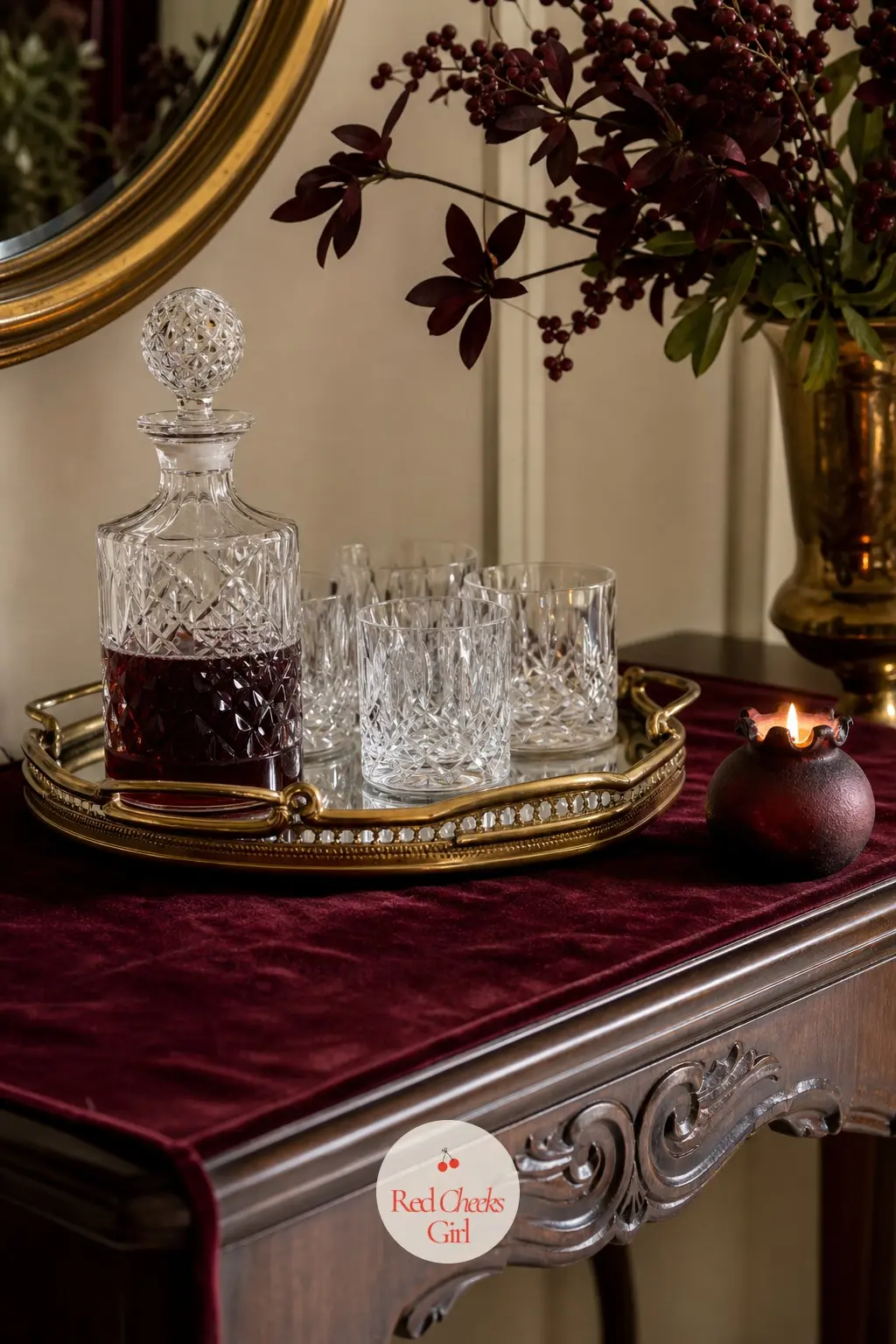 The Entry Console, Set With a Decanter Tray — A burgundy velvet table runner sits under a gold tray holding cut glass tumblers and a decanter, so the first