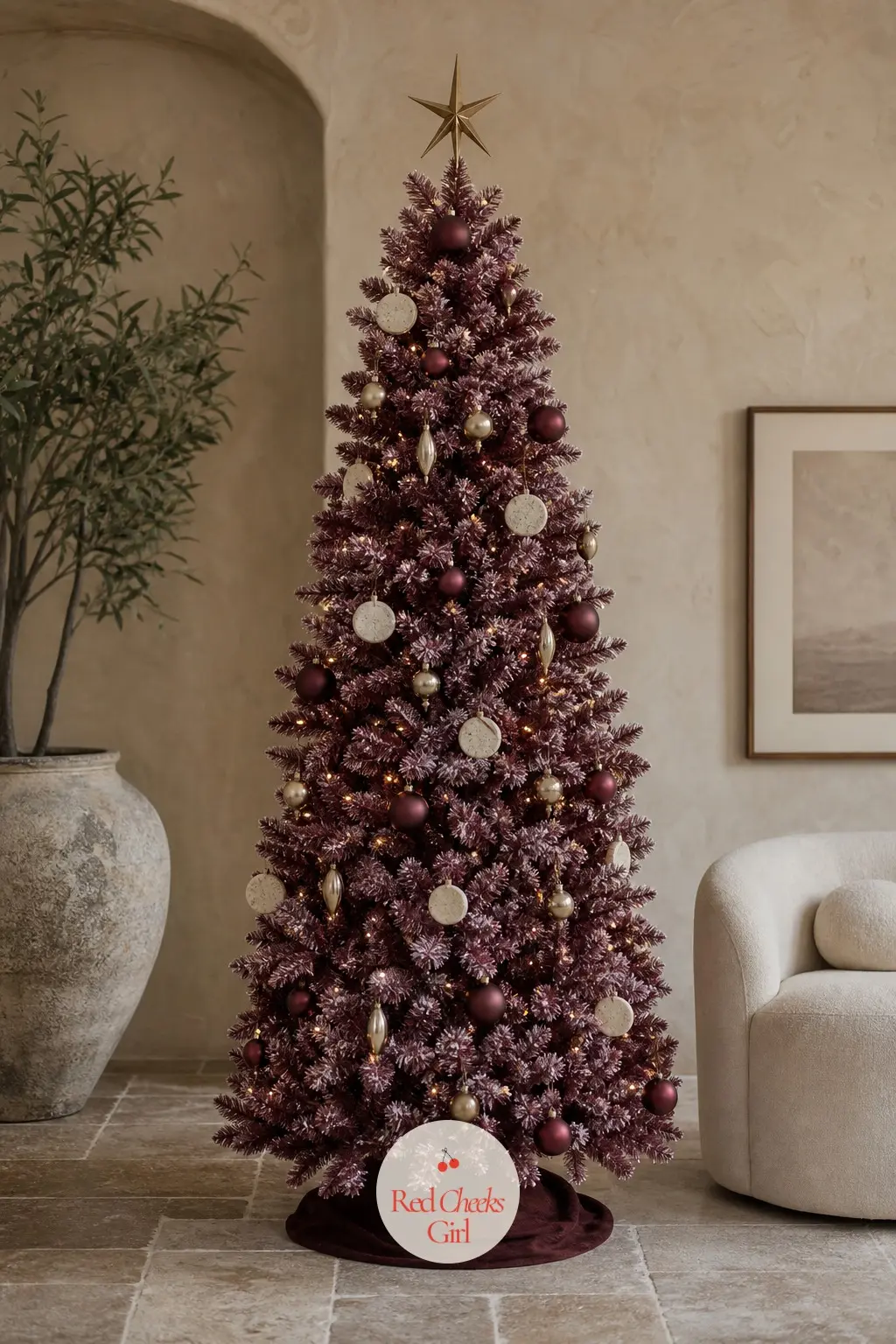 A Matte Burgundy Tree Against Pale Plaster — Flocked matte, not glossy, this artificial tree sits in a pale plaster room with a curved cream chair and a stone