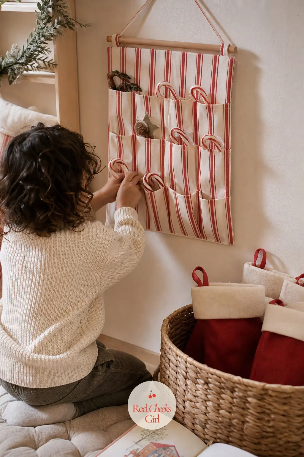 A Kids Corner With An Advent Calendar And A Stocking Each — A small advent calendar in red and white stripe hangs at child height on its own hook, filled with