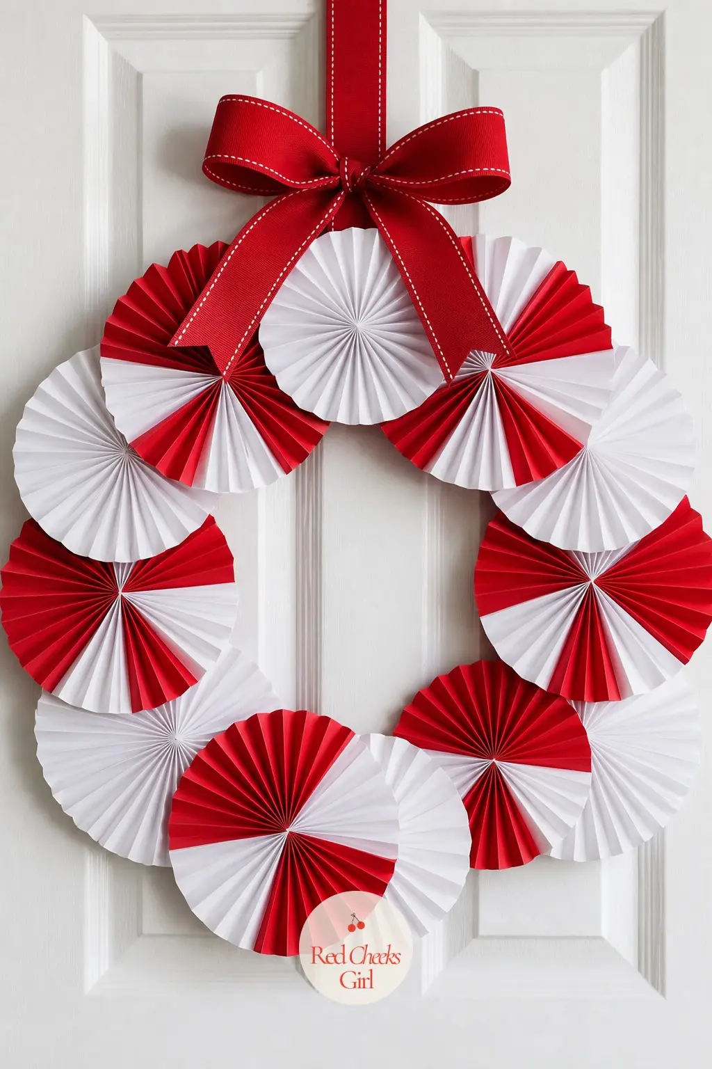 A Paper Fan Rosette Wreath for the Playroom Door — Folded red and white cardstock fans stand on edge around a wire ring, pleated so they catch light like tiny