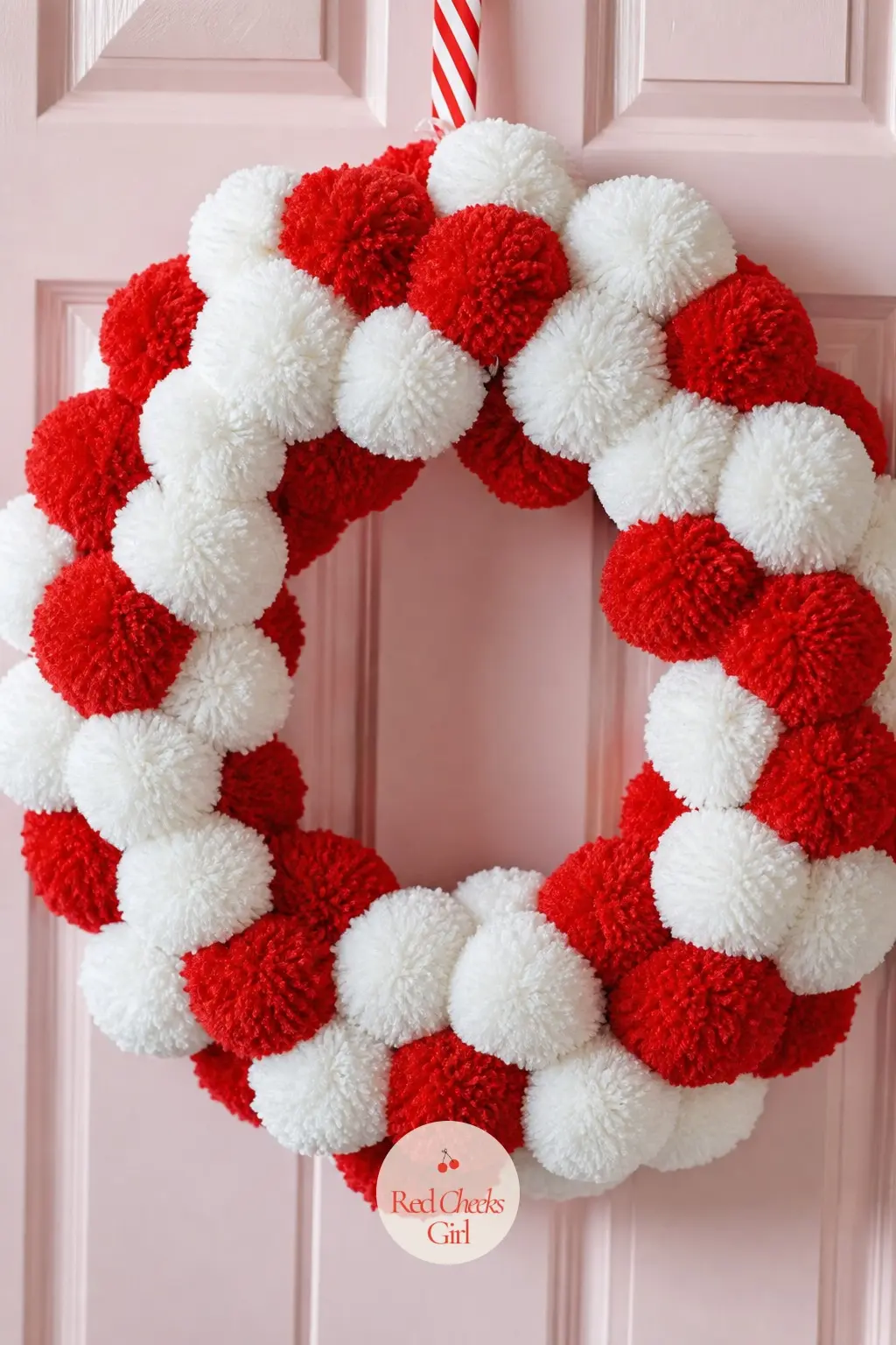 A Red and White Pom-Pom Wreath for the Nursery Closet Door — Soft yarn pom poms in red and white pack edge to edge over a foam ring, with no hard edges, glass