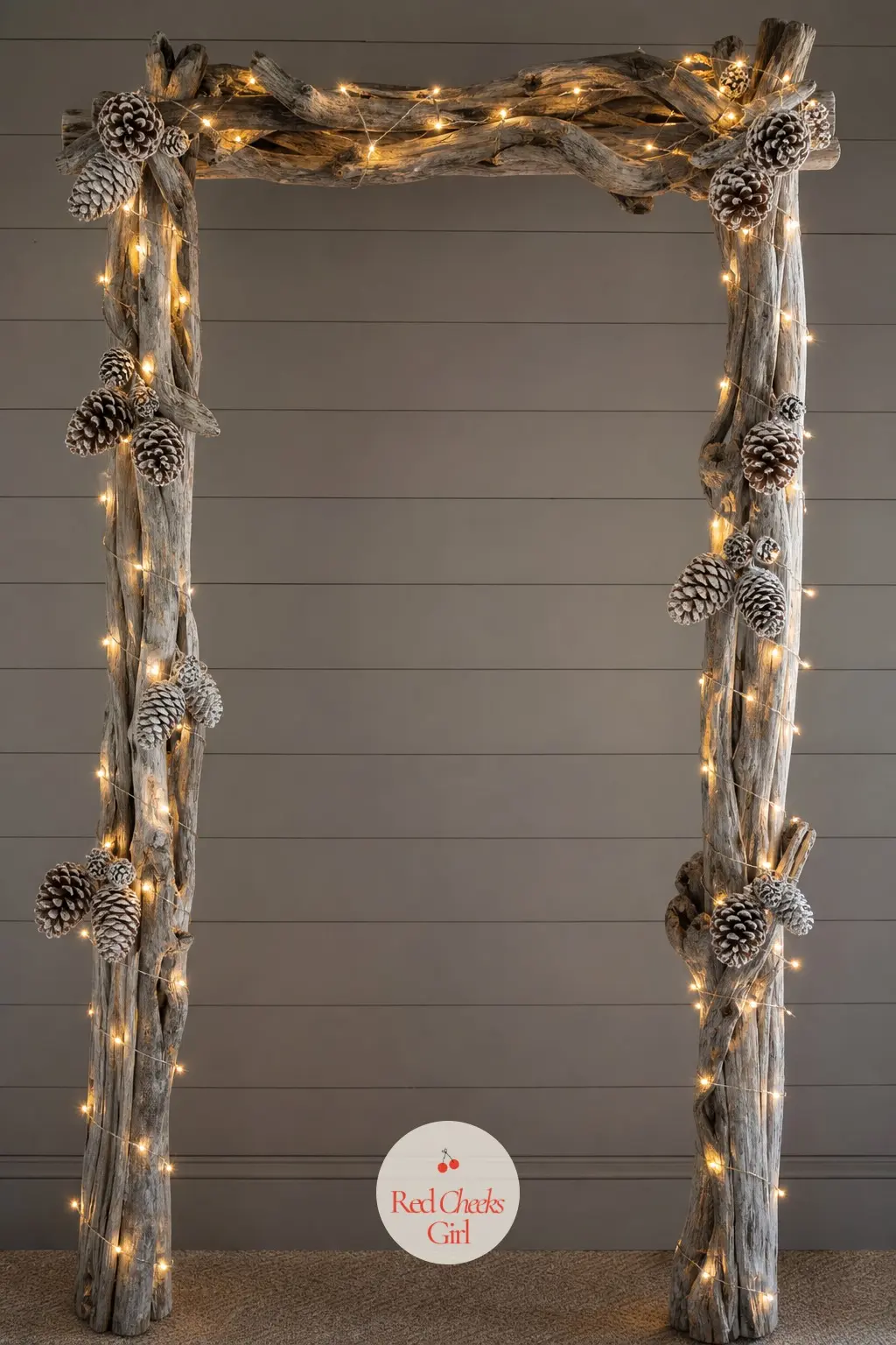 A Driftwood Pole Archway Wrapped in Warm Micro Lights and Frosted Pinecones — A pair of driftwood poles set either side of a doorway, joined with a single