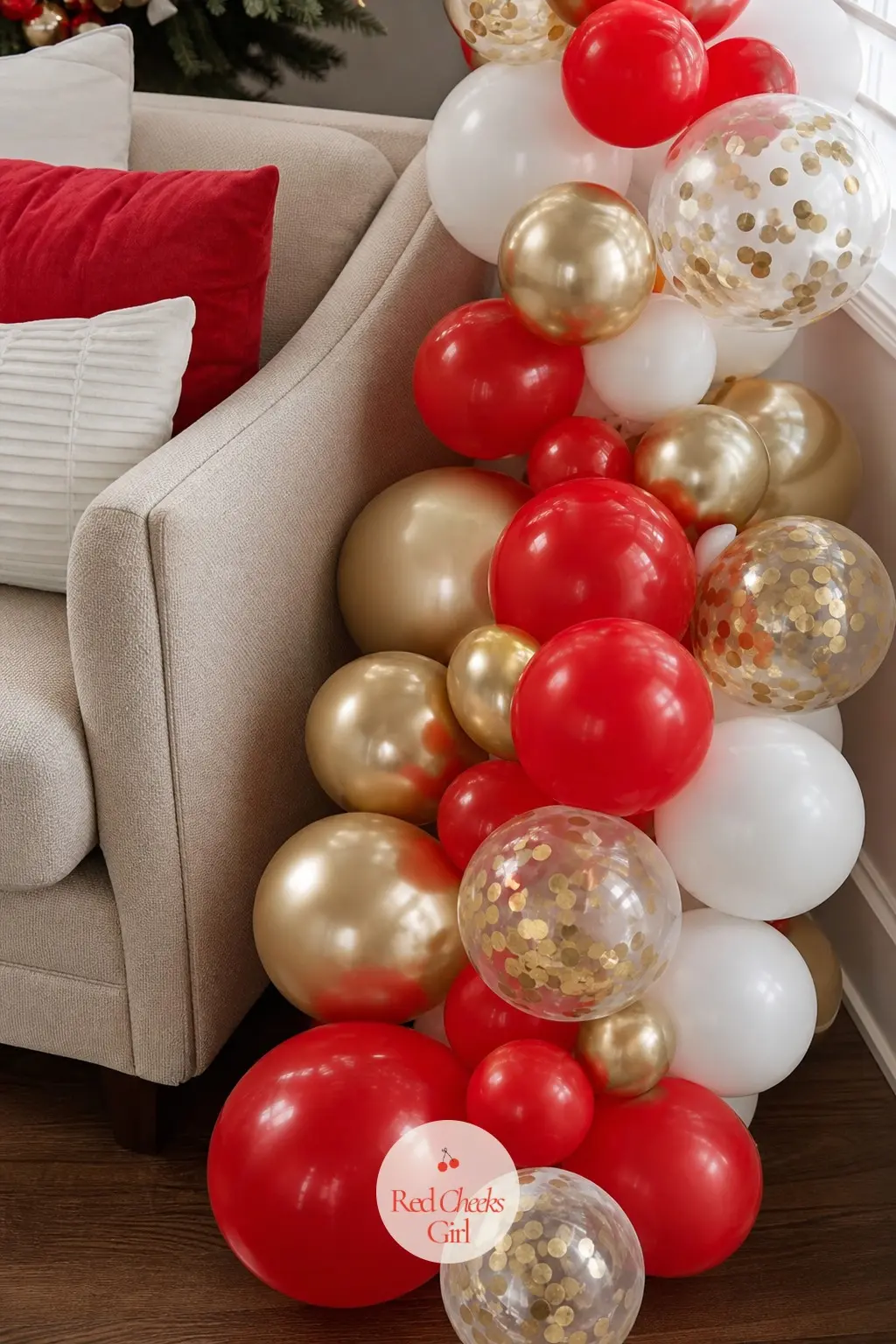 A Floor Garland of Red, White and Gold Balloons Beside the Sofa — A low garland pools along the floor beside the sofa arm rather than hanging at height, giving