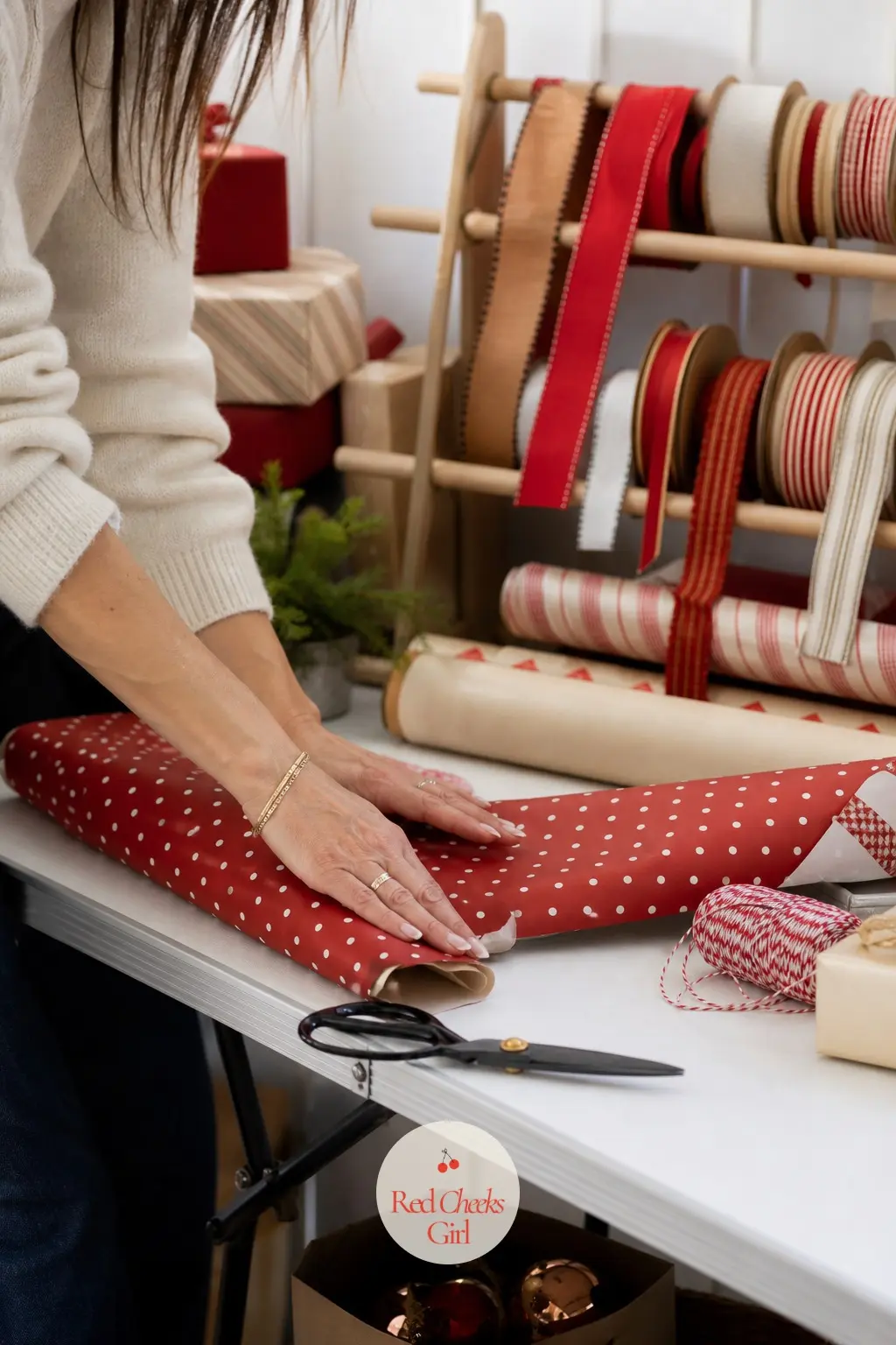 A Folding Table Set Up as a Small Wrapping Station — A narrow folding table against the wall, rolls of cream and red paper stacked on one side and a wooden