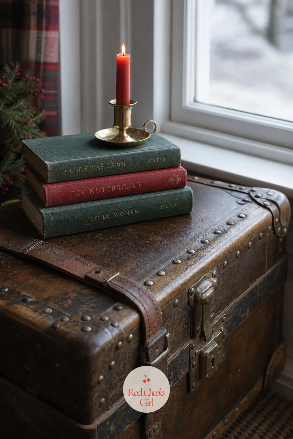 A Vintage Trunk at the Window Topped With Novels and a Candle — A weathered trunk under the window, doing double duty as blanket storage, gets a short stack of