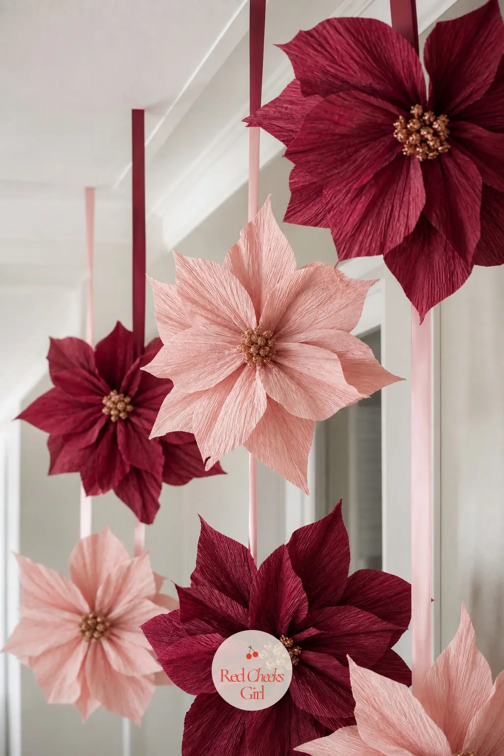 A Row of Oversized Paper Poinsettias in Blush and Wine Suspended at Staggered Heights Down the Hall — Cut poinsettia petals from crepe paper in blush and deep