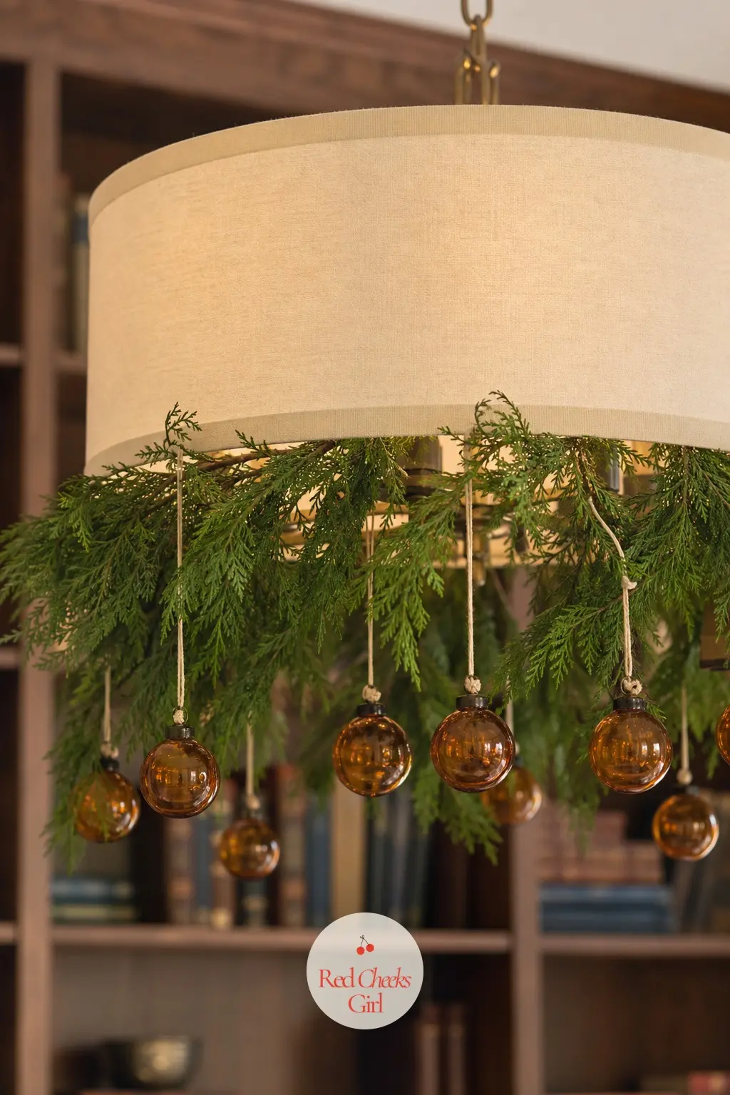 Amber Glass and Juniper Drum Shade Chandelier — An ivory fabric drum shade chandelier in a home library takes well to juniper sprigs ringed around the base
