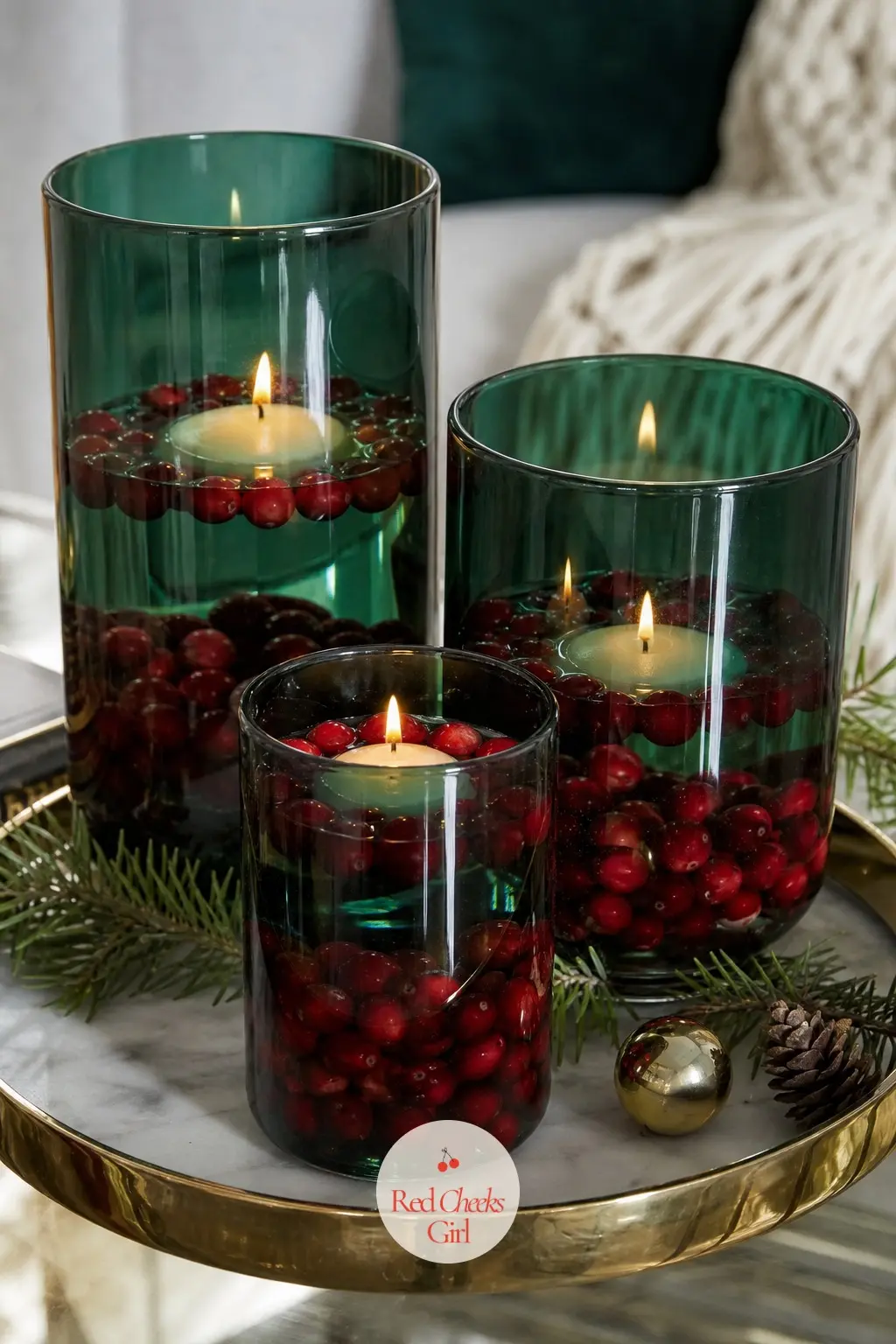 An Emerald Glass Hurricane Trio With Floating Cranberries — Three emerald green glass hurricanes of varying widths each hold a floating candle on a bed of