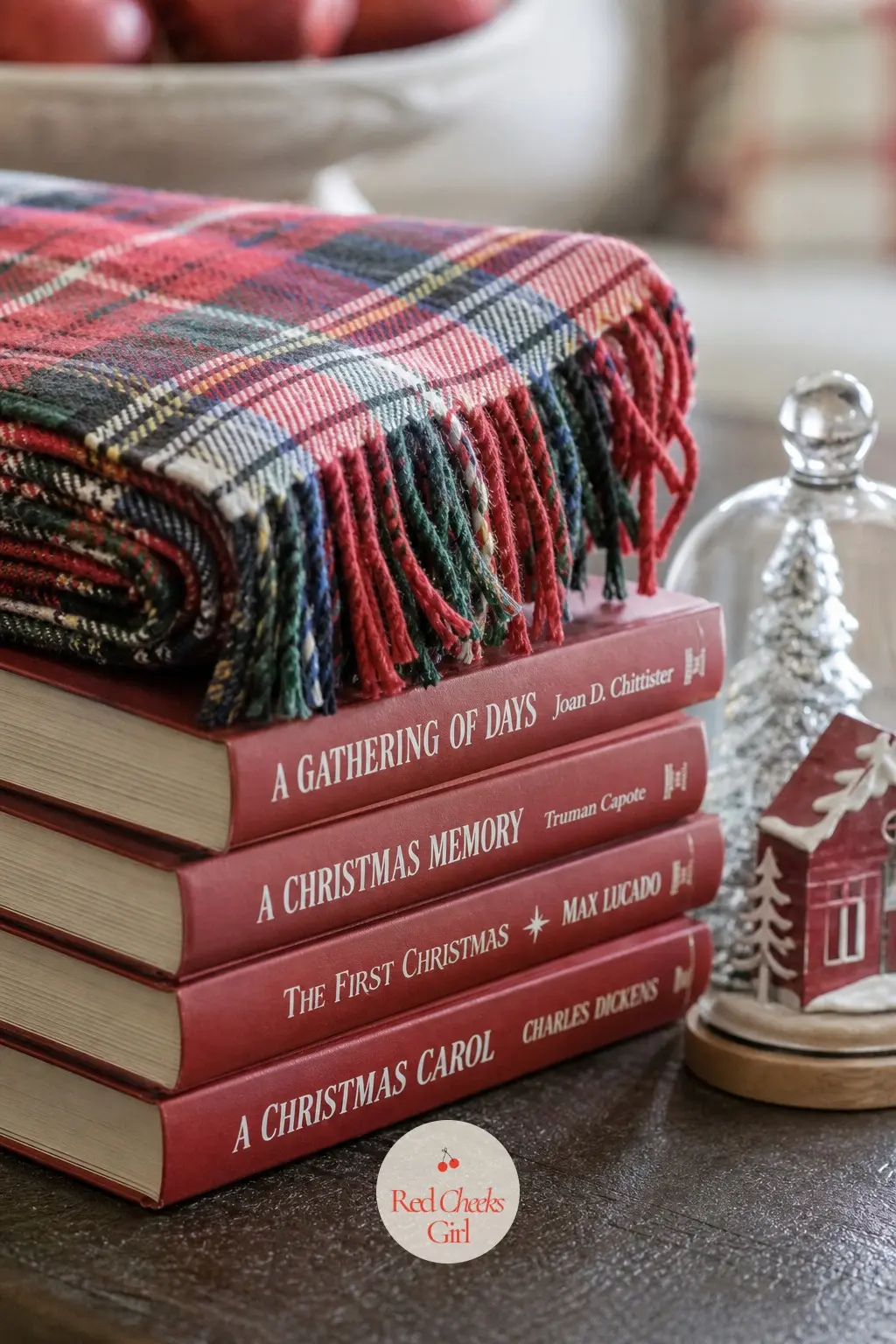 A Stack of Red-Spined Hardcovers Topped With a Plaid Throw Corner — A short stack of hardcover books with deep red spines sits with one corner of a folded