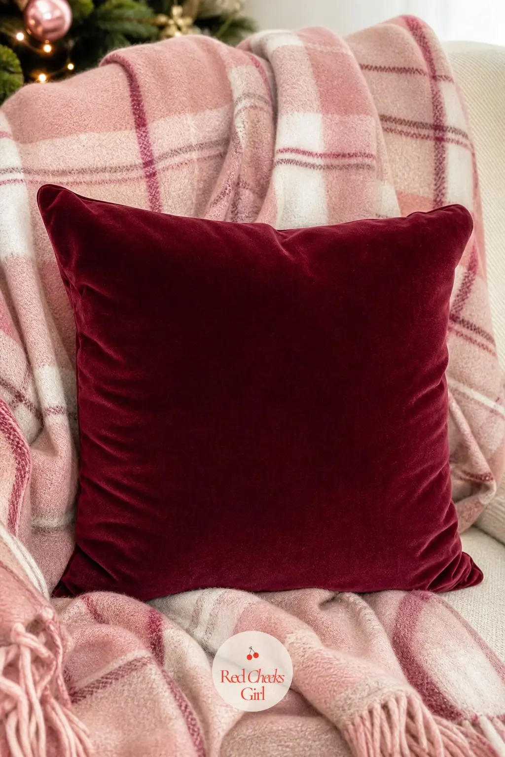 A Wine Velvet Pillow Nested in a Blush Pink Plaid Throw — A blush pink plaid throw, softer and less saturated than a true tartan, drapes loosely over the back