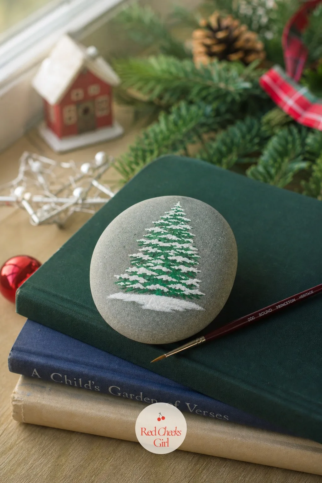 Painted Stone Paperweight — A smooth stone painted with a simple white snow-capped pine tree sits heavy and cool in the hand, holding down a stack of papers on