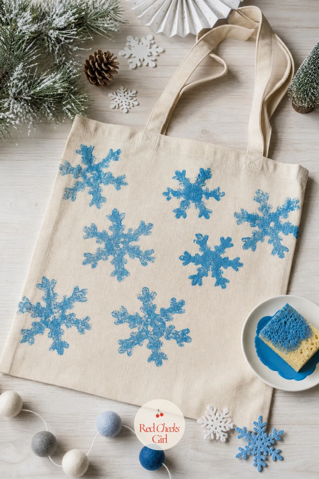 Sponge-Painted Snowflake Tote Bag — A plain canvas tote and a sea sponge cut into a rough snowflake shape let a toddler stamp the same pattern over and over