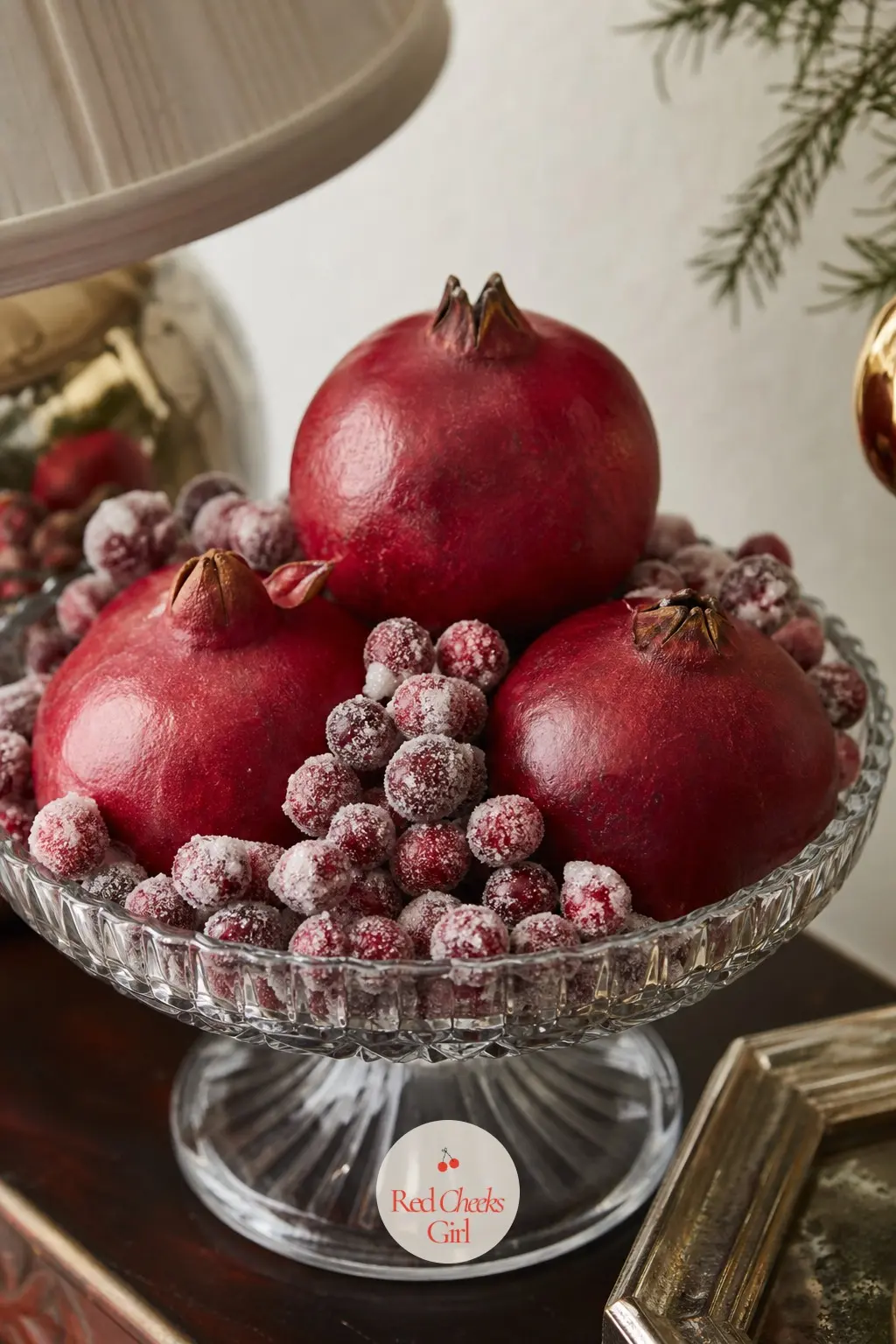 A Bowl of Pomegranates and Sugared Cranberries as a Side Table Finish — A glass compote filled with whole pomegranates and faux sugared cranberries, tucked