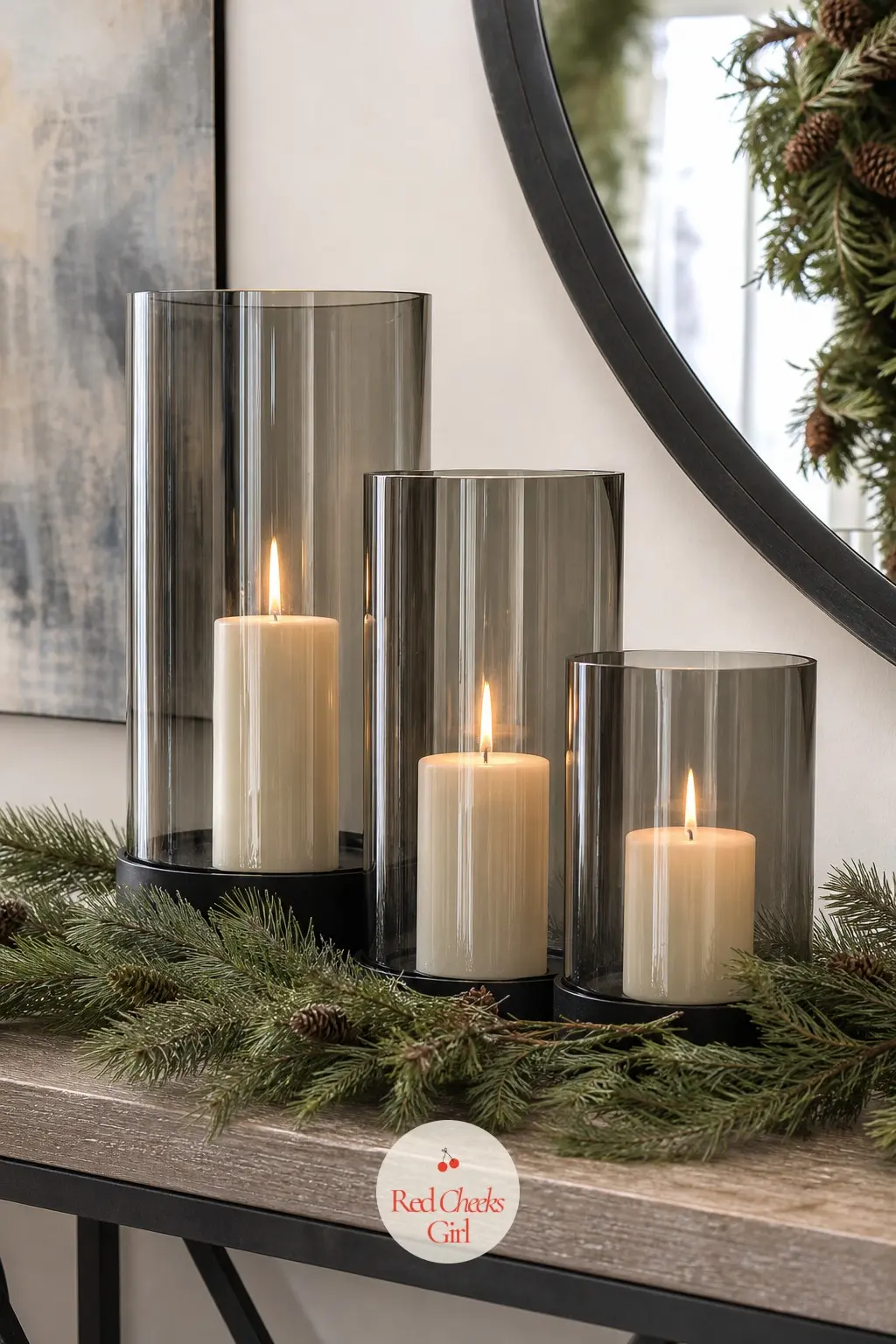 A Console Table Topped with a Trio of Glass Hurricane Lanterns — Three smoked glass hurricane lanterns at graduated heights, each with a pillar candle inside