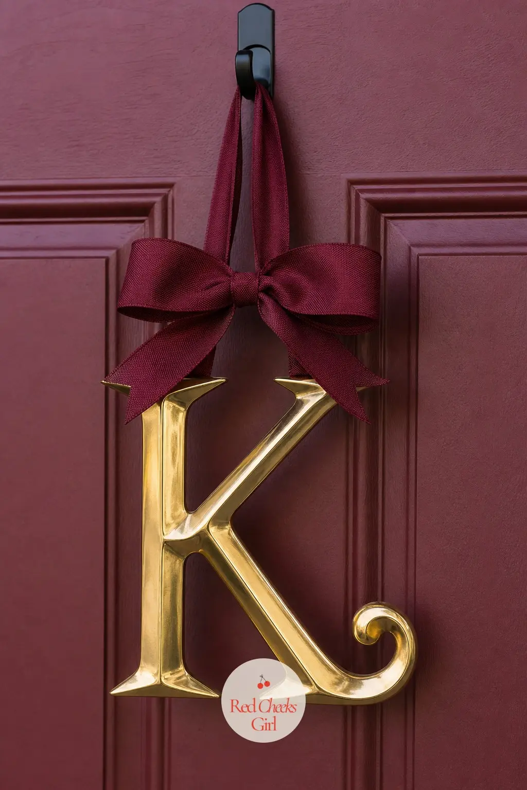 A Gold Metal Monogram Letter on Burgundy Ribbon — A single oversized gold metal letter, the household's initial, hangs from a length of burgundy ribbon off a