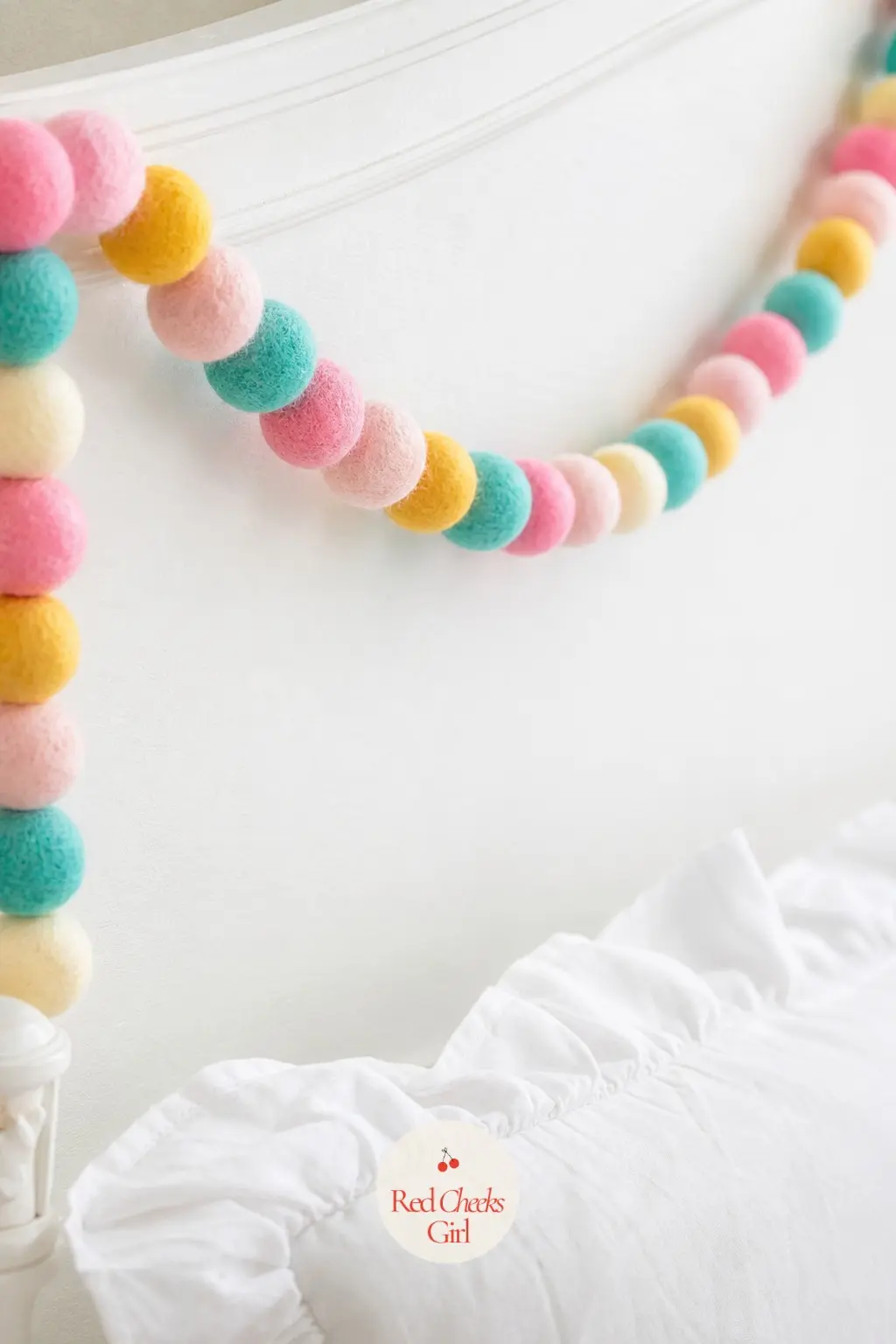 Felt Ball Garland In Candy Colors — A felt ball garland in pink, turquoise and yellow along a bedroom headboard skips Christmas red and green entirely in