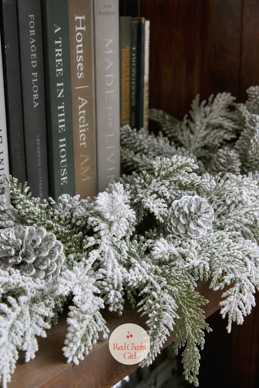 Flocked Greenery With Frosted Pinecones — Snow flocked greenery tucked along a bookshelf with frosted silver pinecones between the books gives a cold, wintry