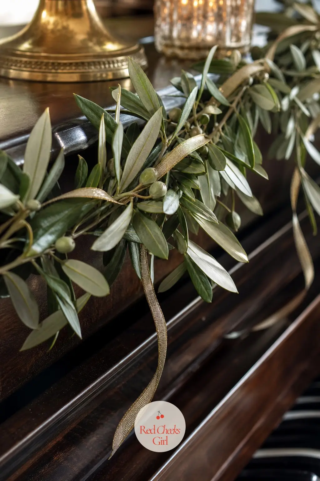 Olive Branch Garland With Gold Ribbon — A slim olive branch garland along a piano top edge, with a thin gold ribbon woven loosely through the silvery leaves