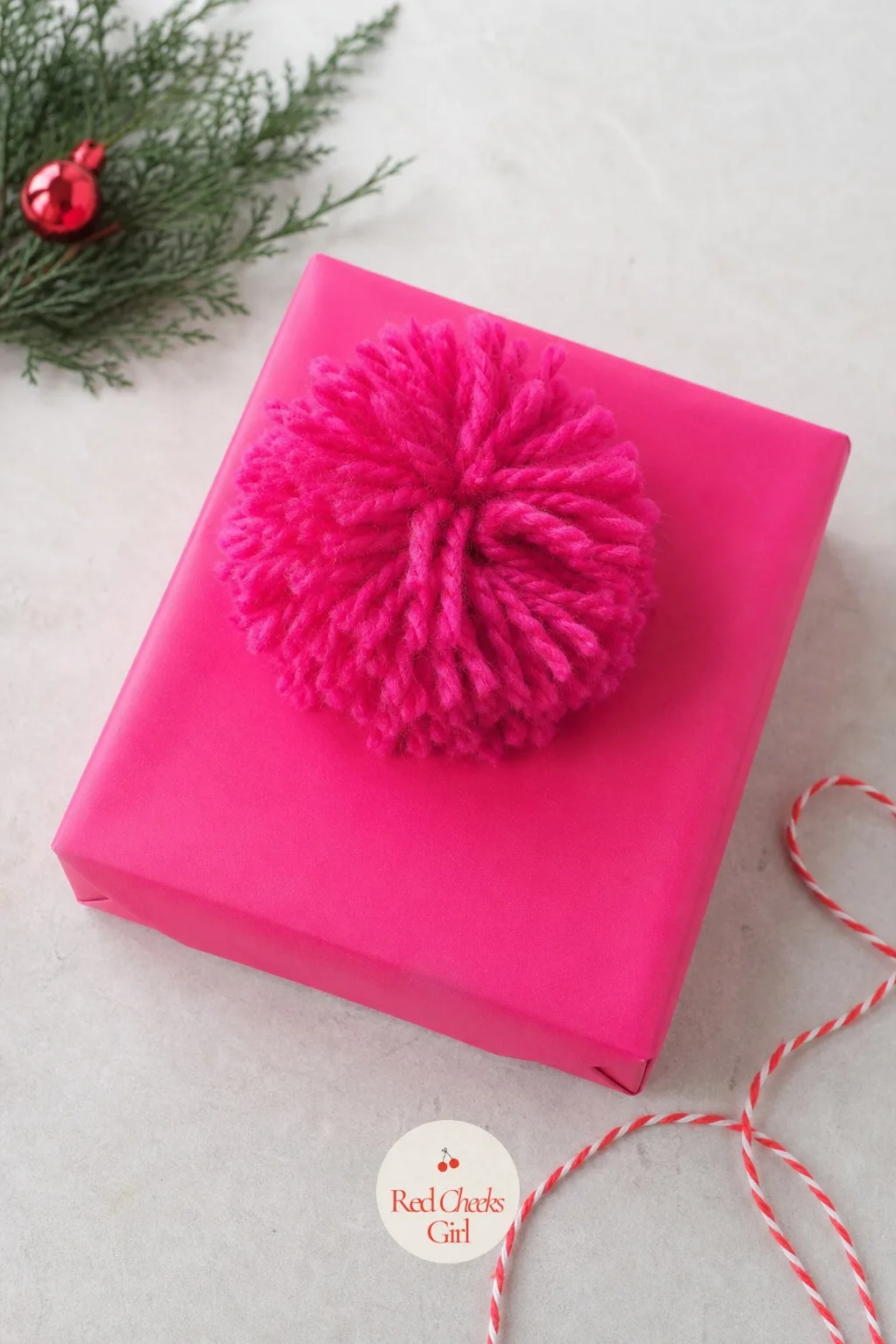 Hot Pink Paper with a Yarn Pompom Topper — This is the wrap for the gift that does not want to behave, bright, a little loud, impossible to lose under a tree