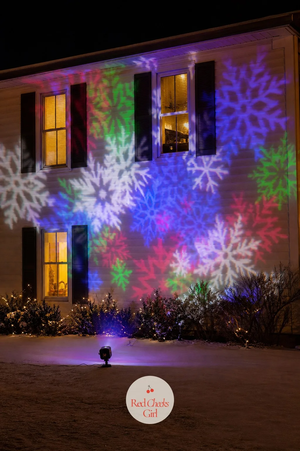 A Holiday Projector Washing the Facade in Color — For the house that would rather not touch the roofline at all, a projector staked into the lawn throws moving