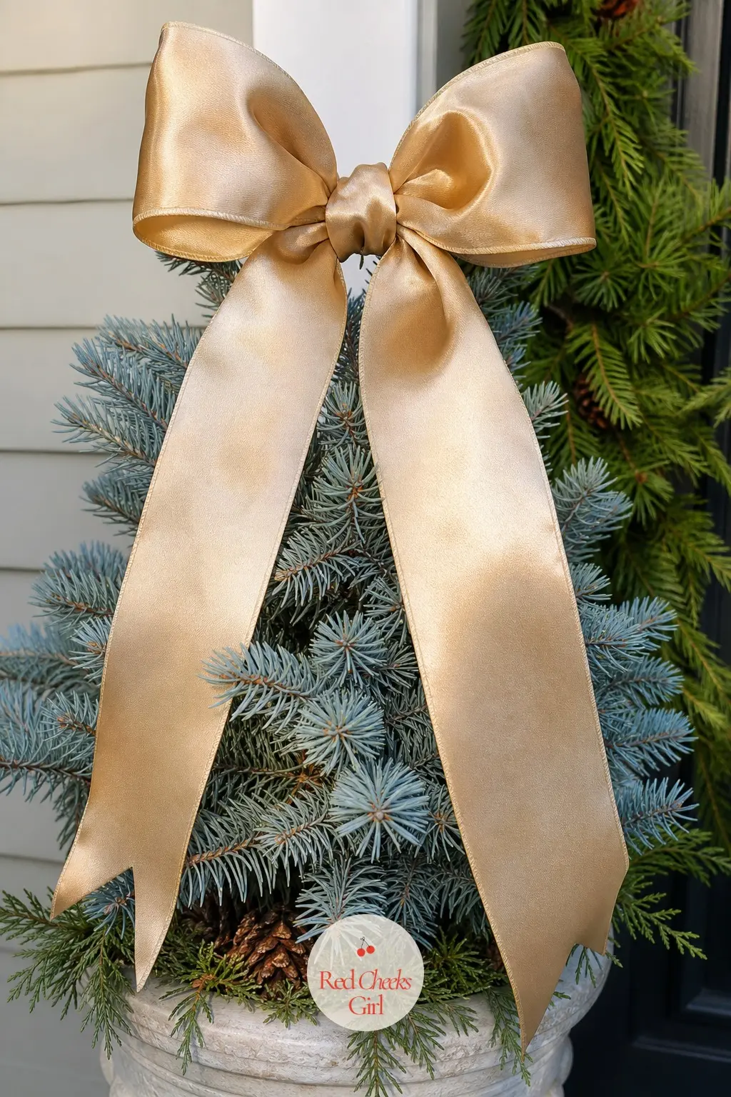 A Giant Champagne Satin Bow Topping a Potted Blue Spruce — A champagne-gold satin bow wired to the top of a small blue spruce gives the tree a finished, almost