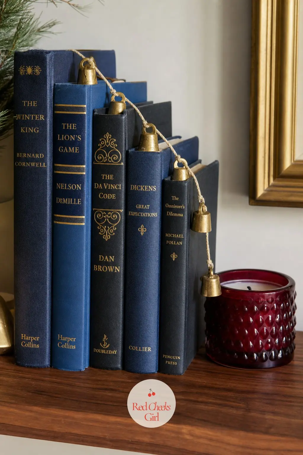 Navy and Gold Book Steps With Brass Bells and a Cranberry Candle — Navy and gold spined books stepped down across the shelf read as rich rather than busy