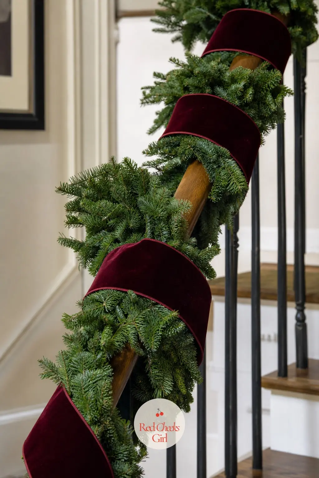 A Noble Fir Rail Garland Spiraled With Wide Burgundy Velvet Ribbon — A full noble fir garland runs the length of the rail, and a wide burgundy velvet ribbon
