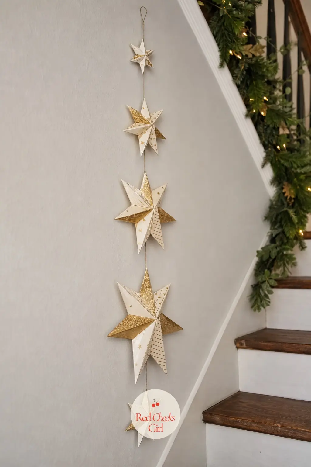 A Staircase Wall Strung With a Vertical Garland of Folded Paper Stars — A line of folded paper stars in cream and gold hangs on fine thread down the staircase