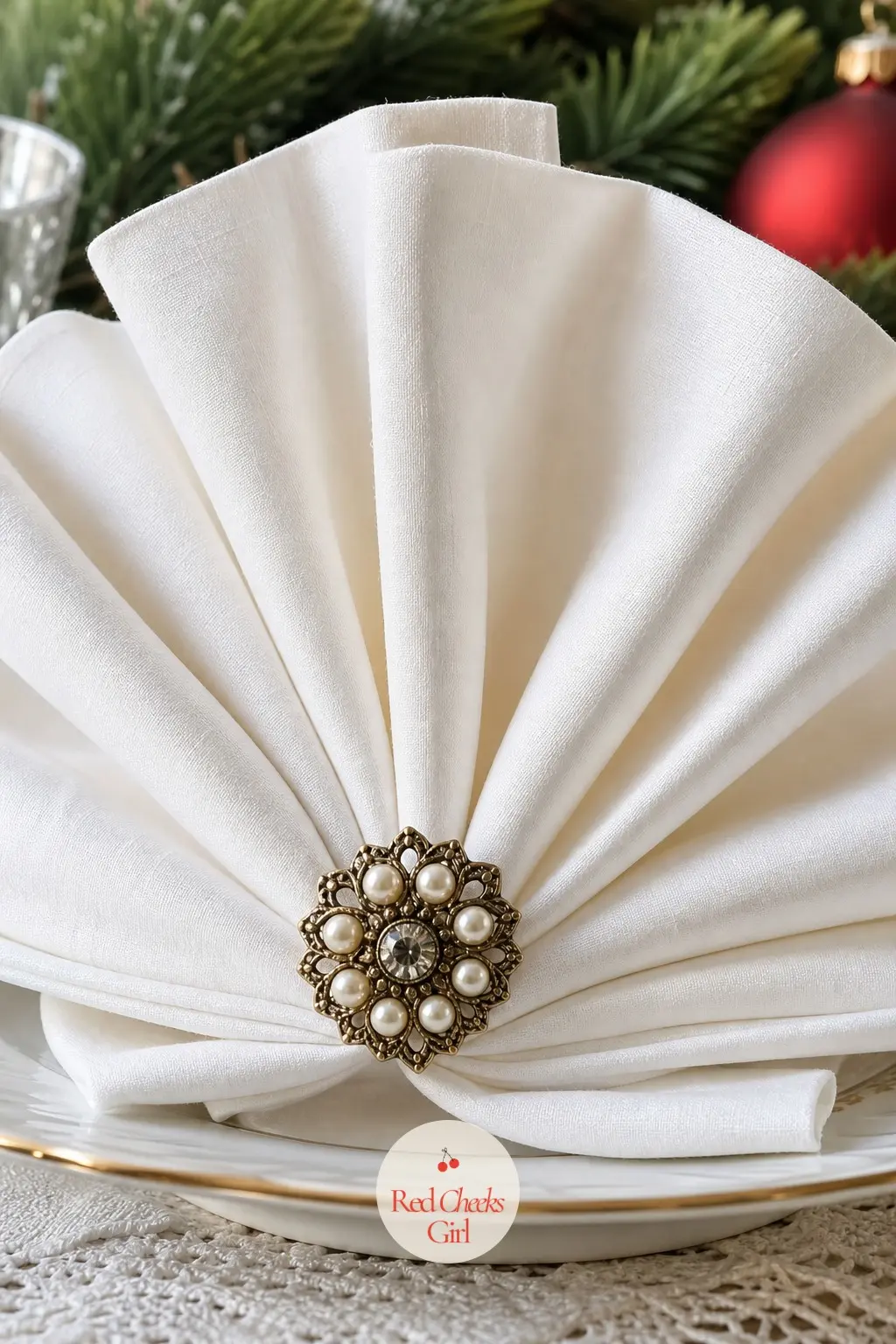 A Linen Napkin Folded Into a Fan and Pinned With a Vintage Brooch — A fan-folded napkin stands upright in a way a flat one never does, and pinning it closed