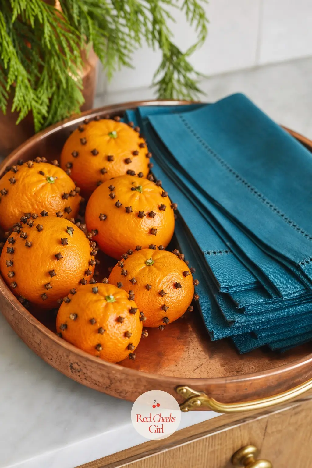 A Copper Tray of Clove Studded Clementines and a Short Stack of Teal Napkins — Whole clementines studded with cloves in a simple pattern sit loose on a round