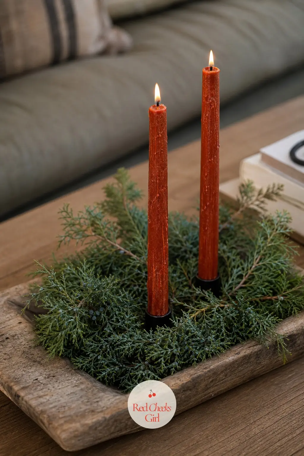 A Weathered Teak Tray of Juniper Sprigs and Hand Dipped Rust Candles — Two short rust coloured candles sit off centre on a weathered teak tray, with loose