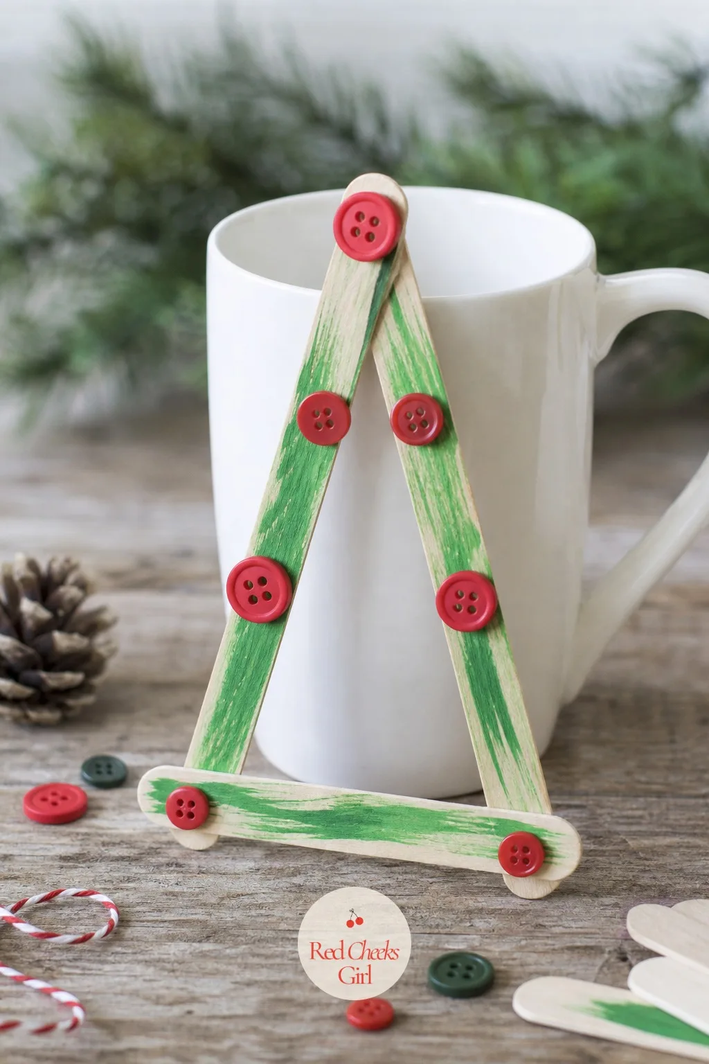 Popsicle Stick A-Frame Tree — Four jumbo craft sticks glued into a simple A-frame, green paint marker streaked across the surface for branches, and a few tiny